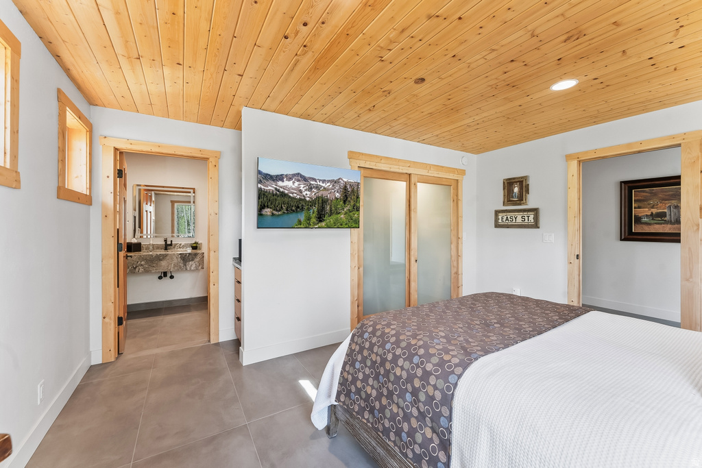 Bedroom featuring a wood-finish plank ceiling, two window openings with wood-finish trim, and large format floor tiling