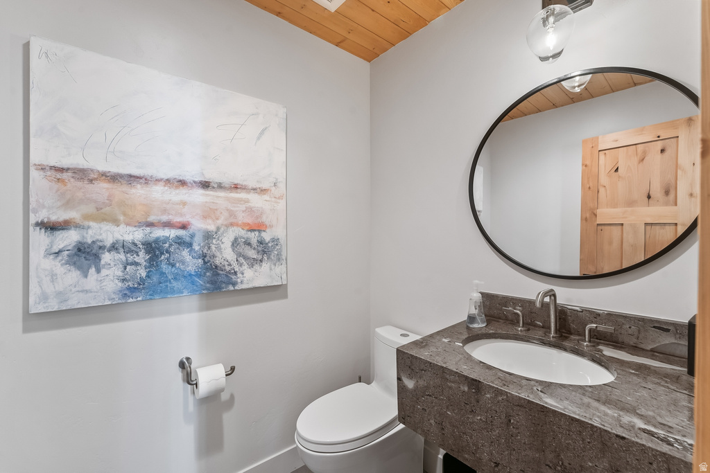 Powder room featuring a wood-paneled ceiling, a dark stone vanity with an undermount sink and brushed nickel faucet, and an oval mirror with a black frame