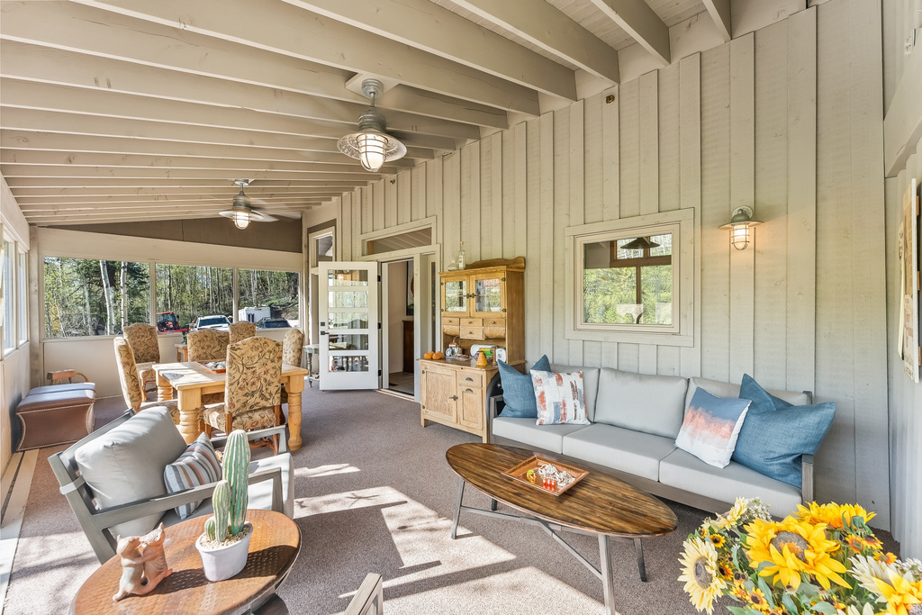 Expansive covered patio featuring a wood-plank ceiling with exposed beams, two ceiling fans, wall-mounted sconce lighting, and board-and-batten siding