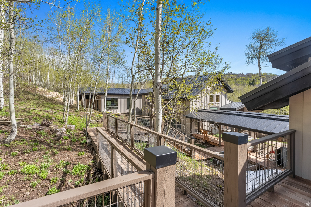 Exterior walkway featuring wood-tone decking and metal cable railing, surrounded by mature aspen trees