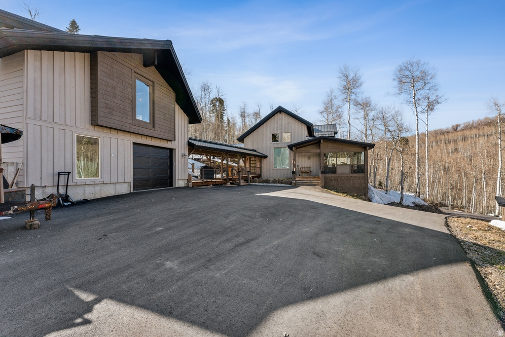 Asphalt driveway providing access to a two-story residence with a dark garage door, vertical siding, and a prominent second-story window