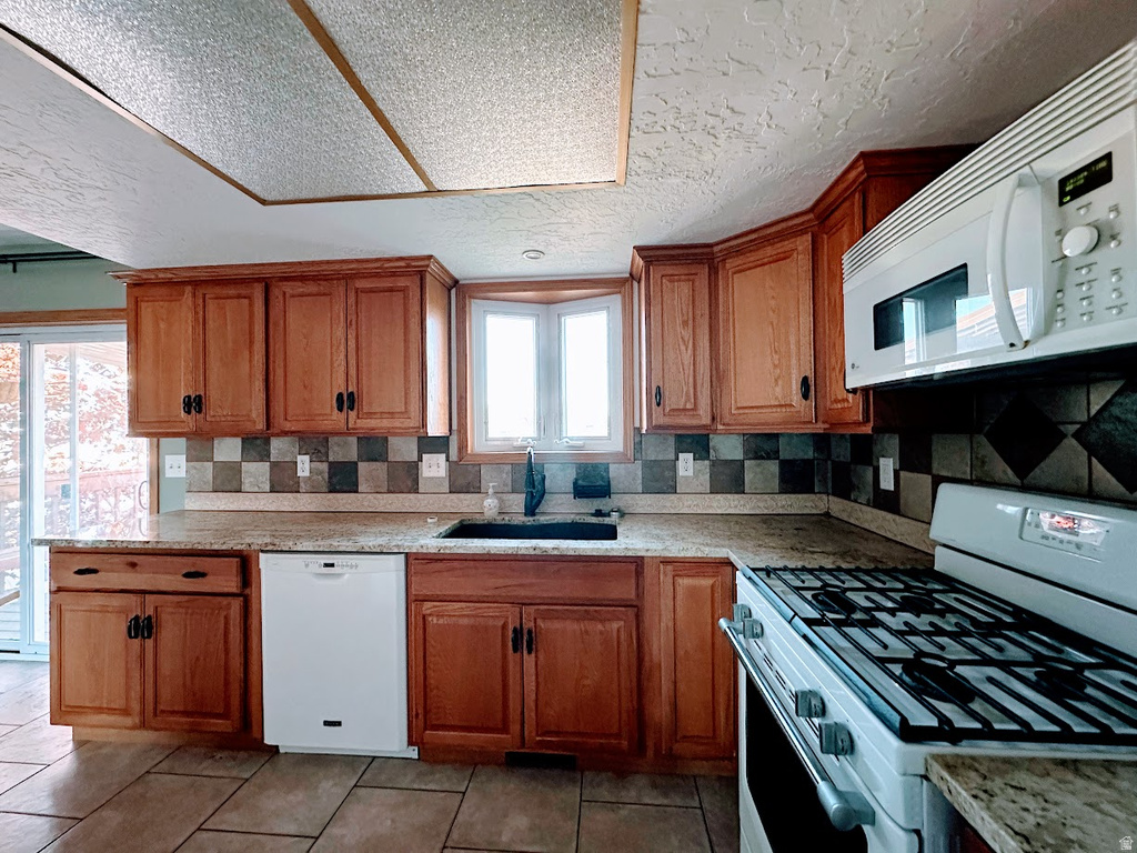 Kitchen featuring wood cabinetry, a bay window, a built-in microwave, a gas range, and a tiled backsplash