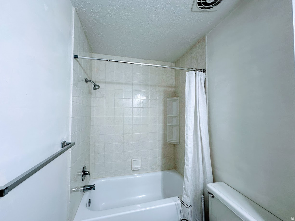 Bathroom featuring a white bathtub, ceramic wall tiling, shower head with dark-finish fixtures, and an integrated shower caddy