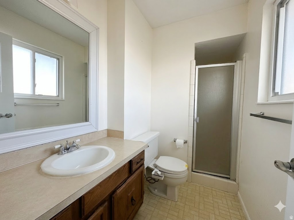 Bathroom featuring an integrated sink vanity with wood-finish cabinetry, a framed mirror, a privacy glass shower enclosure, and light-toned floor tiling