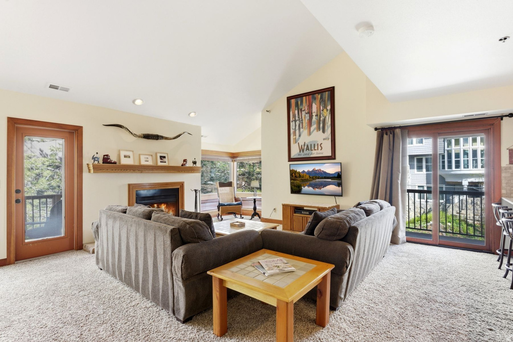 Living area featuring vaulted ceilings, a built-in fireplace with wood mantel, and plush carpeting