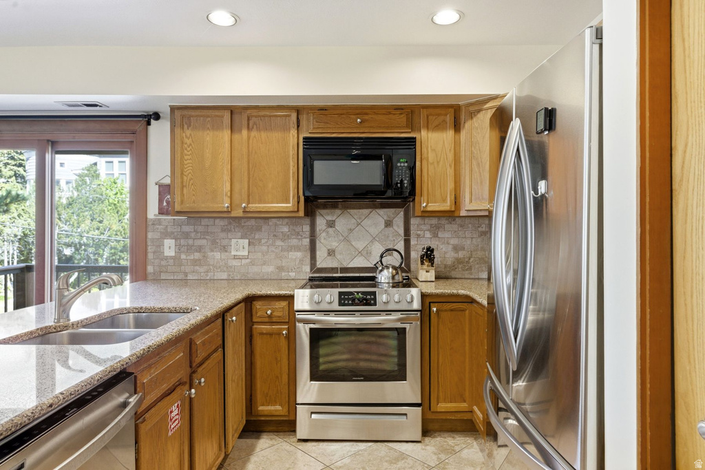 Kitchen featuring wood cabinetry, stainless steel appliances, speckled countertops, and a tiled backsplash