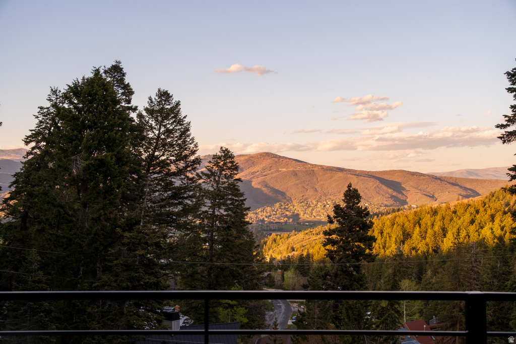 Expansive mountain landscape with a verdant forest, visible from a balcony featuring a black metal railing