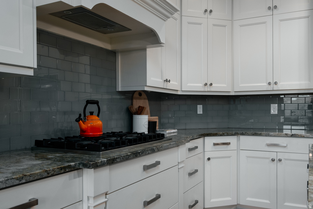 Kitchen featuring white cabinetry with silver-tone hardware, a built-in gas cooktop, natural stone countertops, and a subway tile backsplash