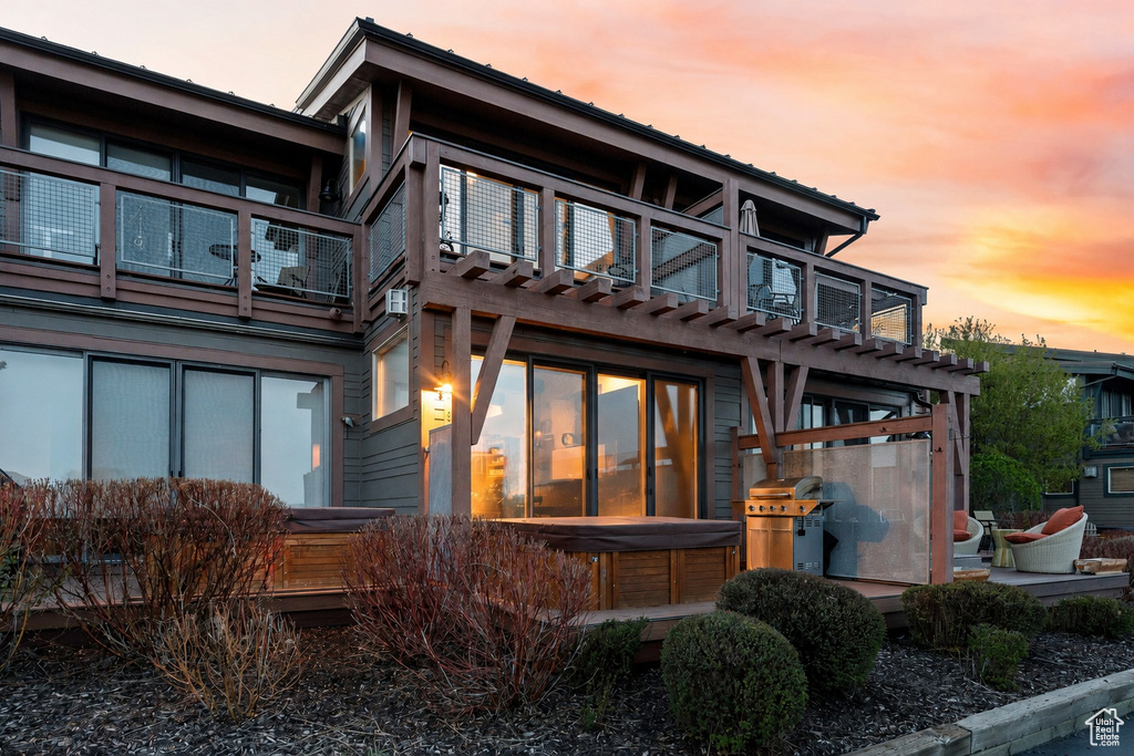 Multi-level exterior featuring a ground-level deck with a built-in hot tub, an overhead wooden pergola, and upper-level balconies with glass and metal railings