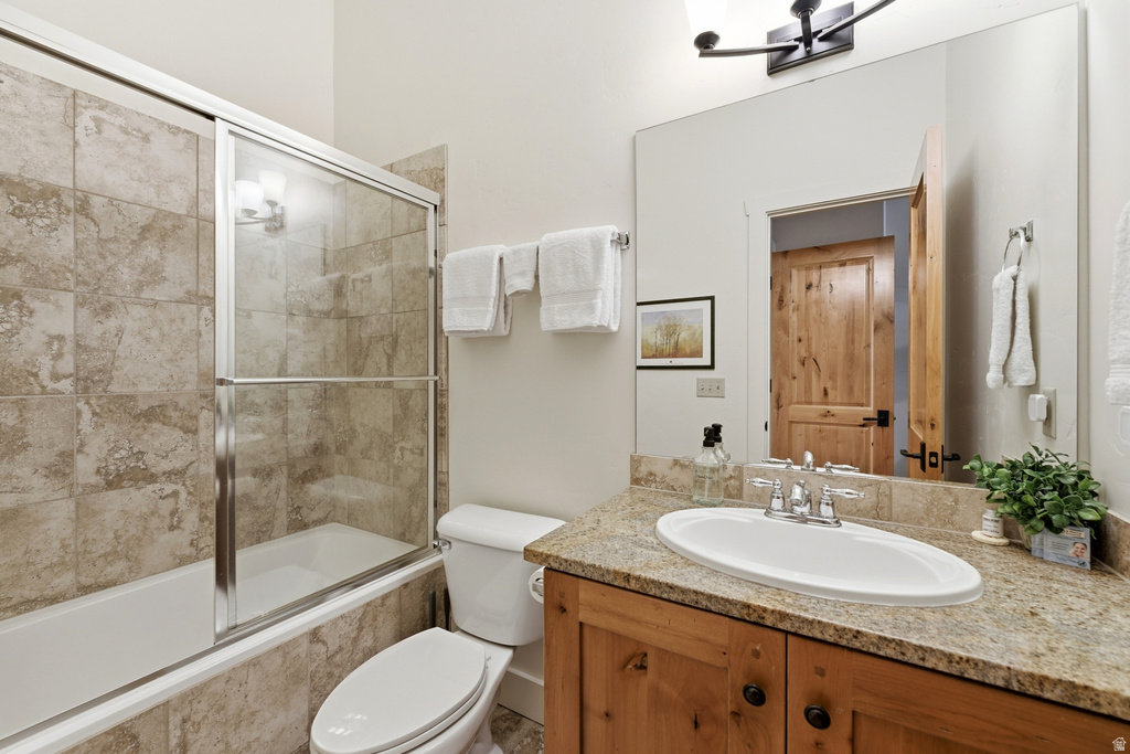 Bathroom featuring a full-size bathtub with glass sliding doors, stone tile surround, wood-finish vanity with an undermount sink, granite-style countertop, and a large wall-mounted mirror