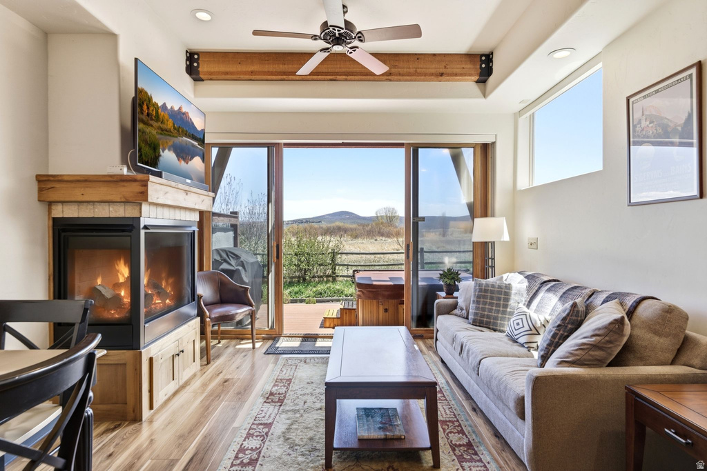 Spacious living area featuring a fireplace with stone surround and wood mantel, wood-finish flooring, and a ceiling fan