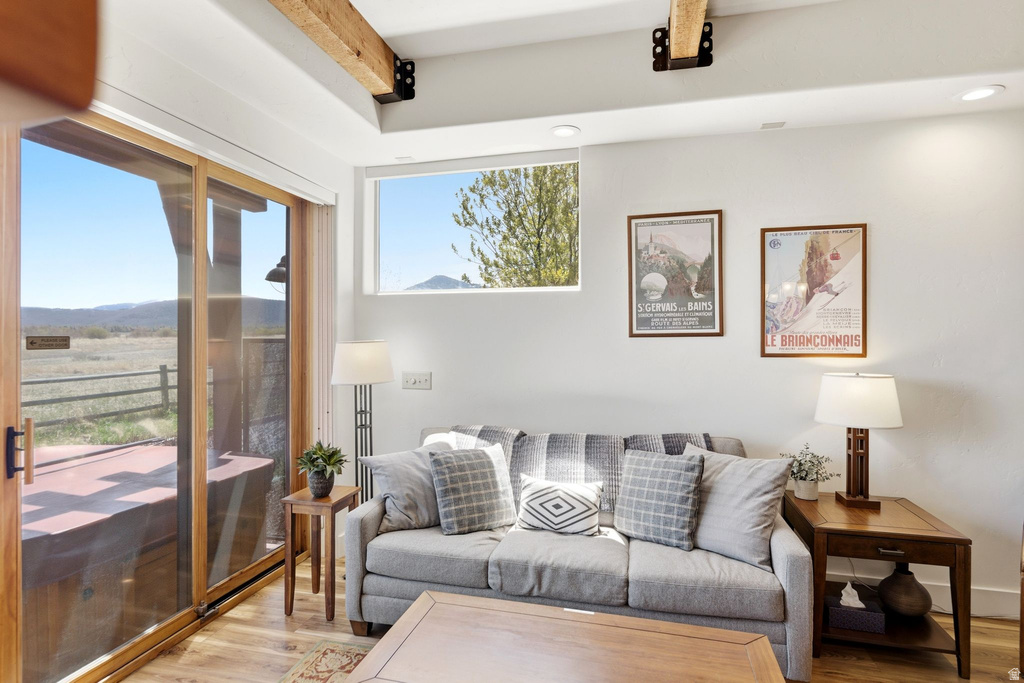Living area featuring a sliding glass door, high transom window, exposed wood ceiling beams, recessed lighting, and wood-finish flooring