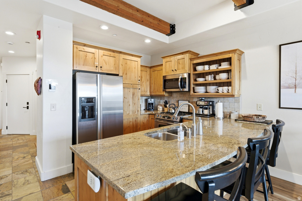 Kitchen featuring light wood cabinetry, stainless steel appliances, a tile backsplash, and a granite countertop island with integrated sink