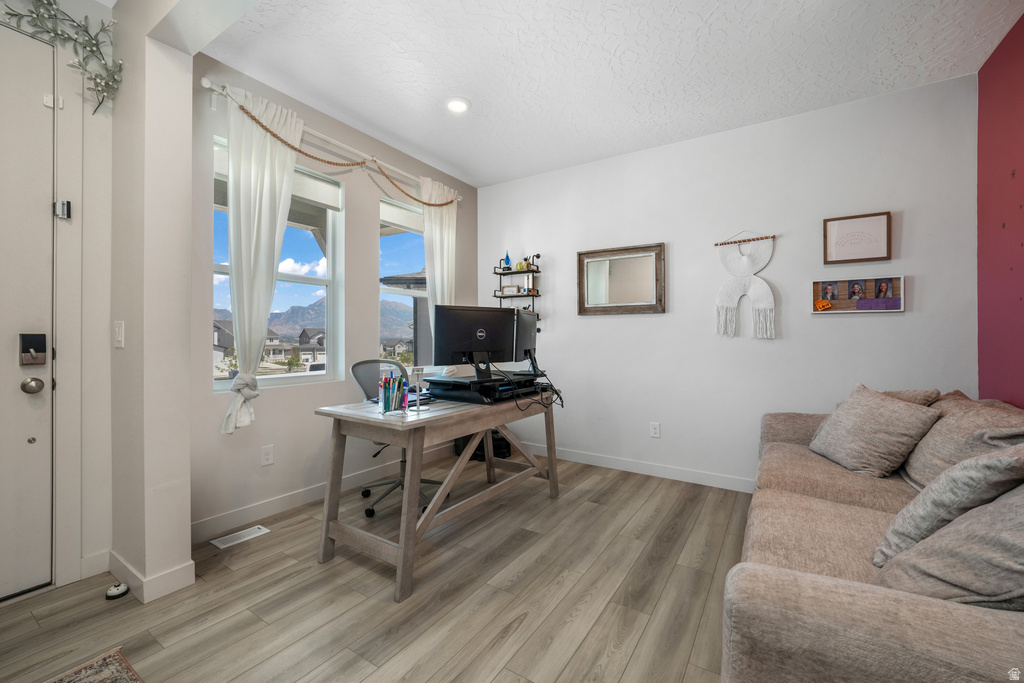 Spacious room with light wood-finish flooring and multiple windows, featuring a recessed light fixture and a contrasting accent wall