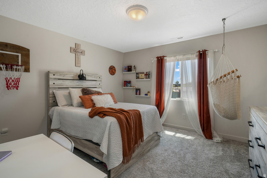 Carpeted bedroom featuring a window with sheer and opaque drapes, a ceiling-mounted light fixture, and built-in shelving