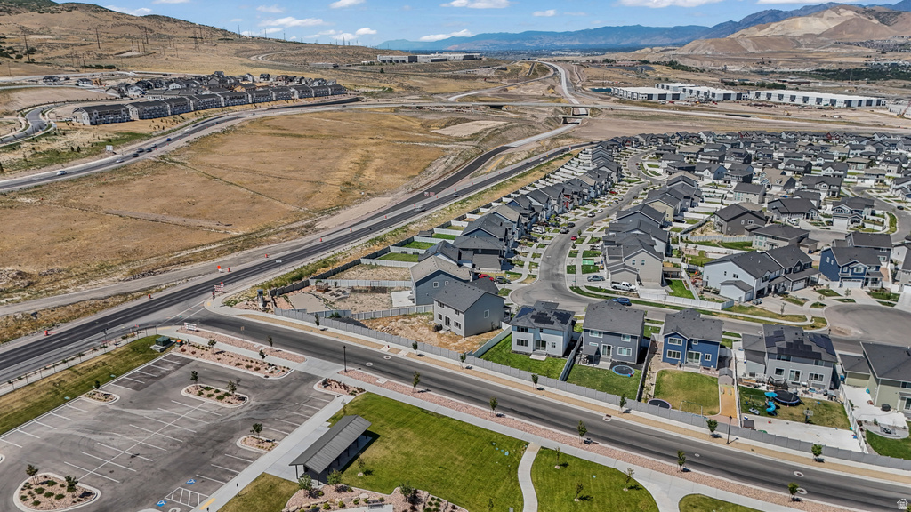 Expansive aerial perspective showcasing a residential development with multiple single-family homes, mountain backdrop, paved roadways, and a community park area with a parking lot