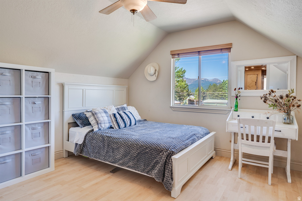 Bedroom featuring vaulted ceilings, wood-finish flooring, and a window with mountain scenery