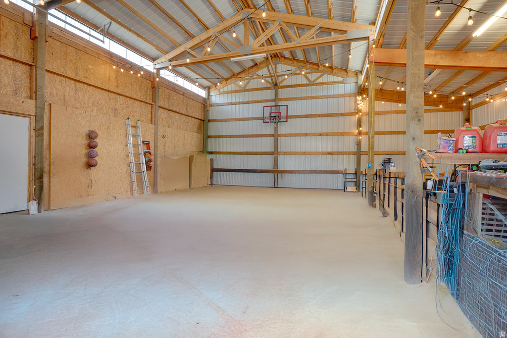 Spacious interior structure featuring exposed timber framing, a corrugated metal roof, high ceilings with ambient string lighting, and a concrete floor