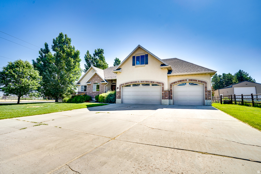 Two-story residence featuring a stucco and brick exterior, two garage doors with arched stone detailing, a prominent dormer window with shutters, and a wide concrete driveway