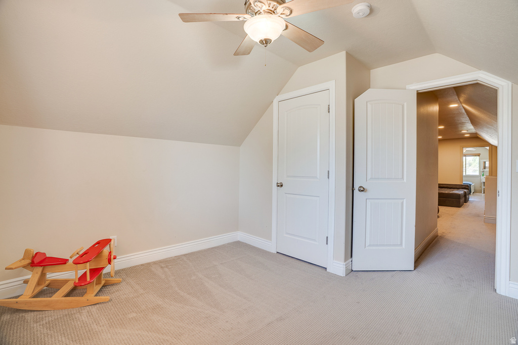 Carpeted room with sloped ceilings, a ceiling fan with integrated lighting, and white baseboards