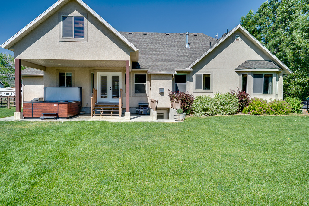 Spacious rear yard with a covered patio, French doors, and a built-in hot tub