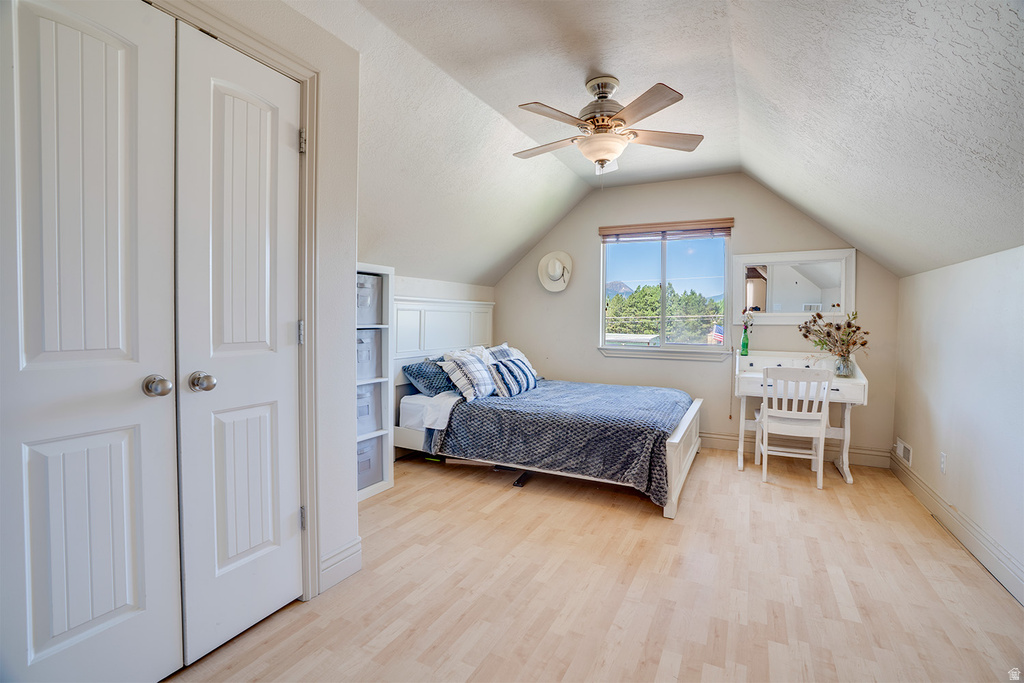 Spacious room featuring light wood-finish flooring, a window with mountain scenery, and an angled ceiling with a ceiling fan