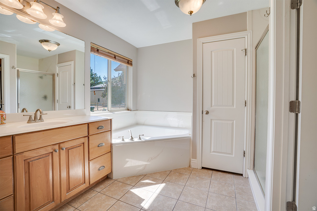Corner soaking tub with a large window, complemented by an expansive wood-finish vanity with dual sinks, a large mirror, and tiled flooring