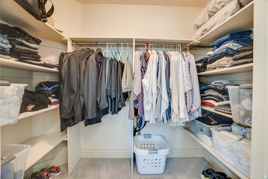 Walk-in closet featuring white built-in shelving, multiple hanging rods, baseboard trim, and light gray carpet flooring