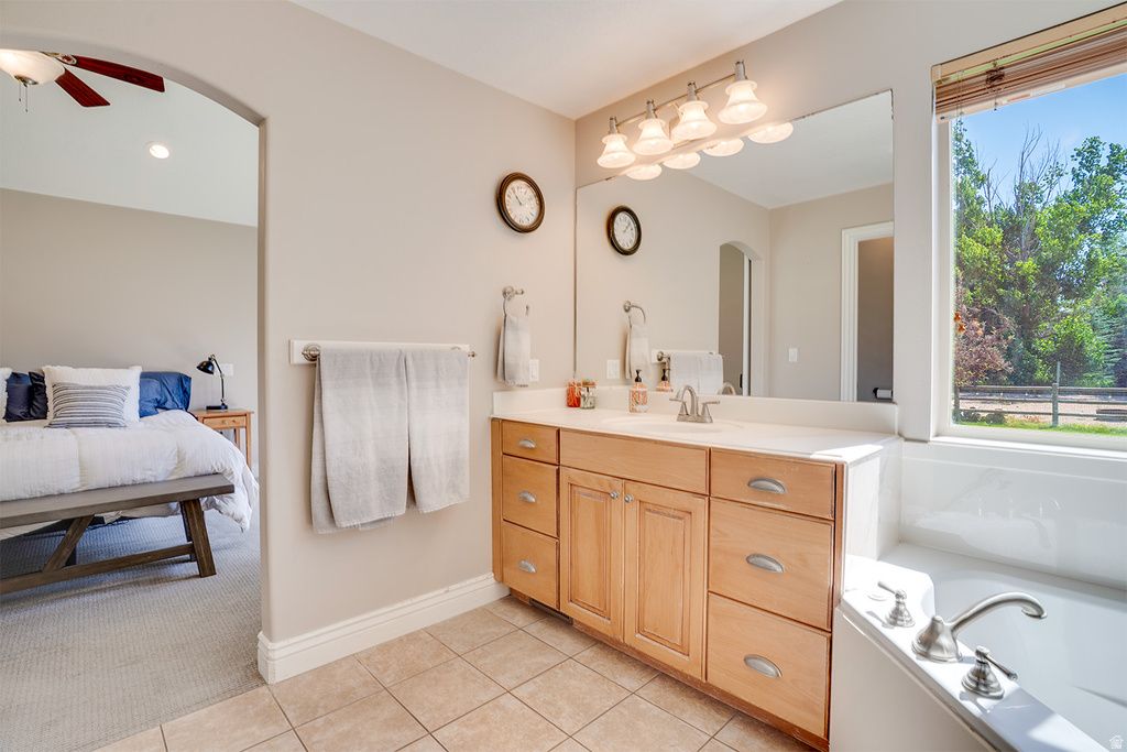 Bathroom featuring a light wood-finish vanity with a light-toned countertop, a large mirror, and a built-in bathtub with a window