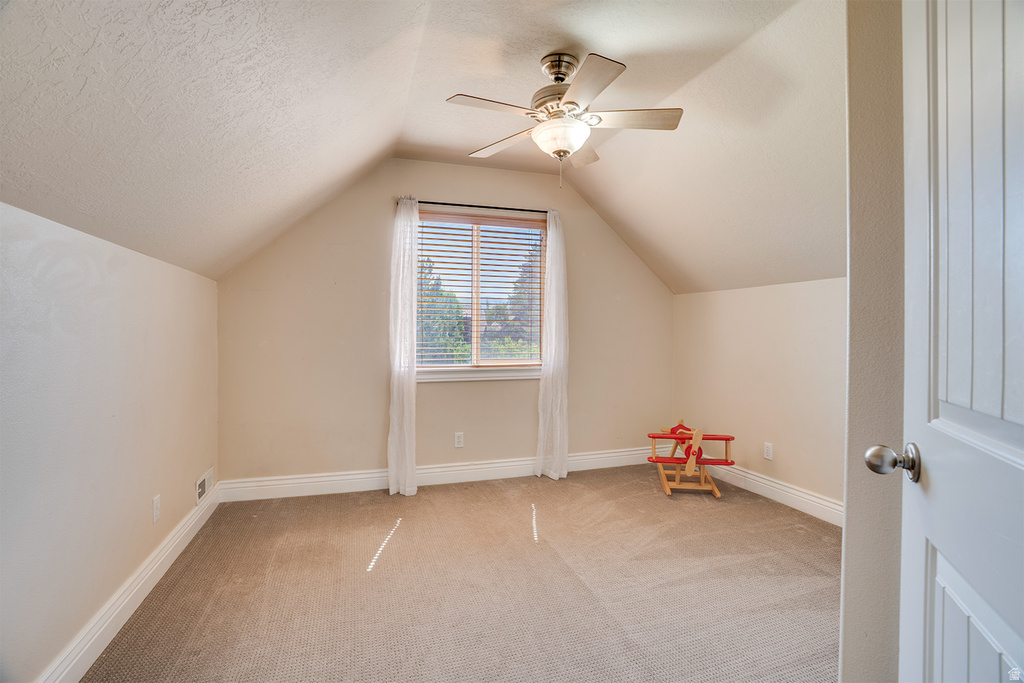 Carpeted room with sloped ceilings featuring a window with blinds, a ceiling fan with integrated lighting, and white baseboards