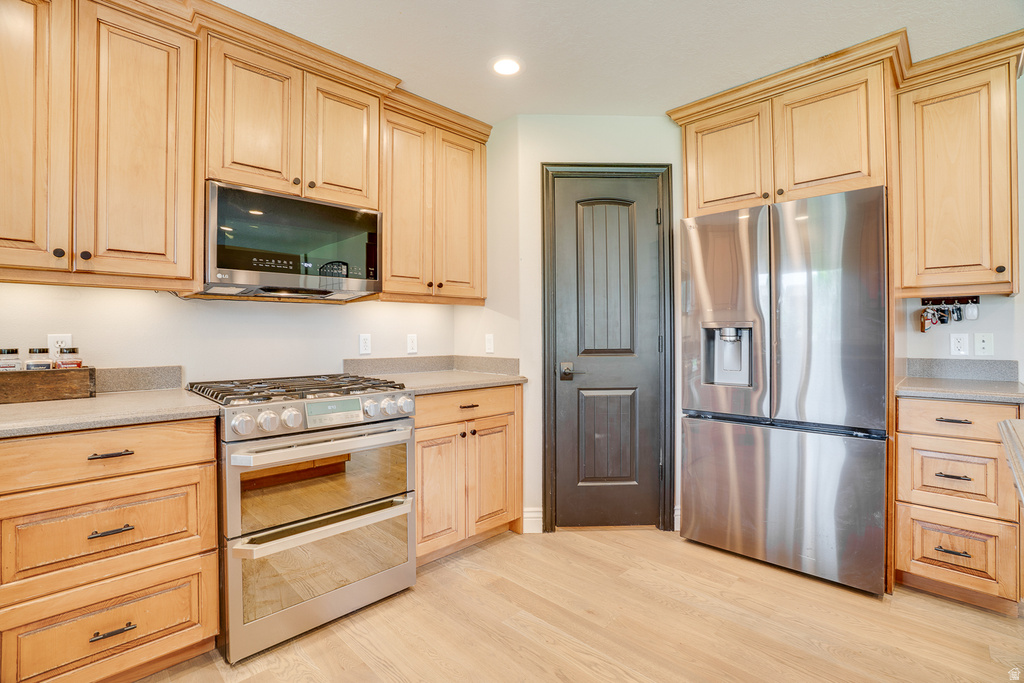 Kitchen featuring light wood cabinetry with dark hardware, stainless steel appliances, stone countertops, and wood-finish flooring