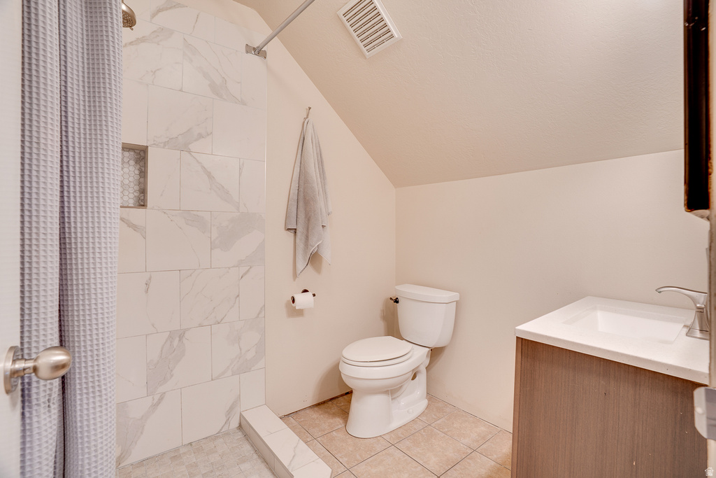 Bathroom featuring a shower with large format white tile, a built-in shower niche with honeycomb tile, a single vanity with an integrated sink, and an angled ceiling