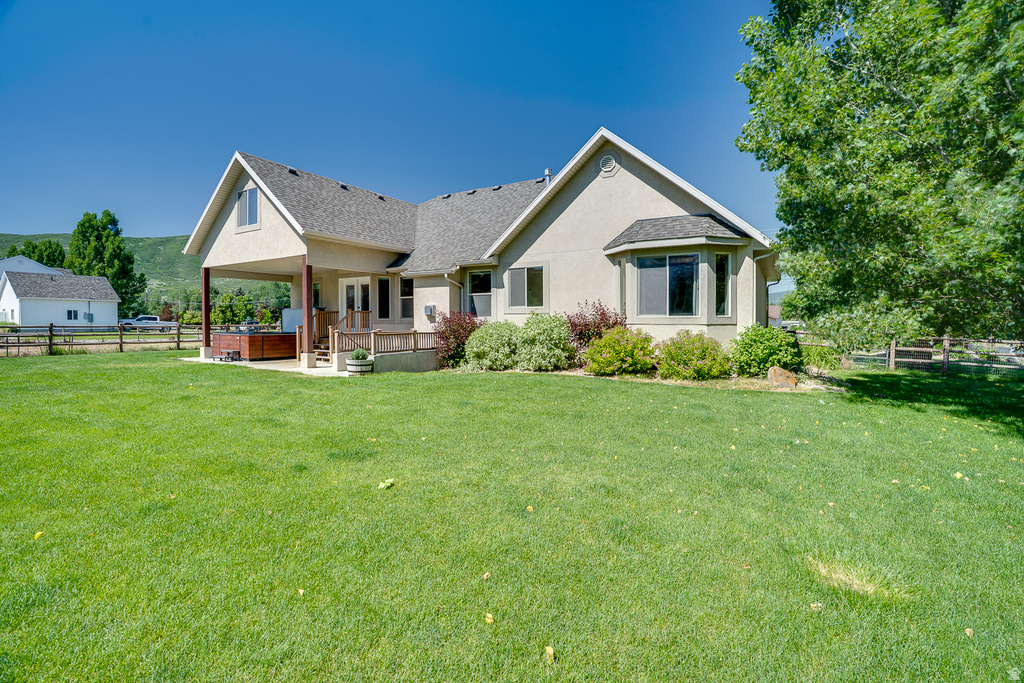 Expansive green lawn bordering a stucco exterior home featuring a covered patio, recessed hot tub, and a bay window