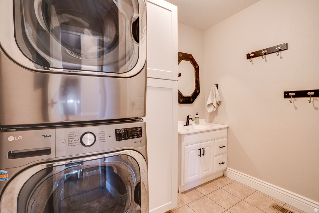Laundry space featuring stacked stainless steel appliances, white cabinetry, and tile flooring