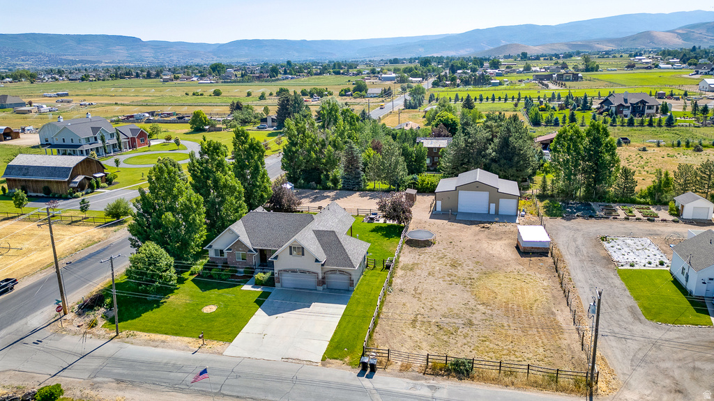 Expansive property featuring a single-story residence with an attached three-car garage, a detached metal-sided outbuilding with two roll-up doors, a large paved driveway, a manicured front lawn, and mature perimeter trees