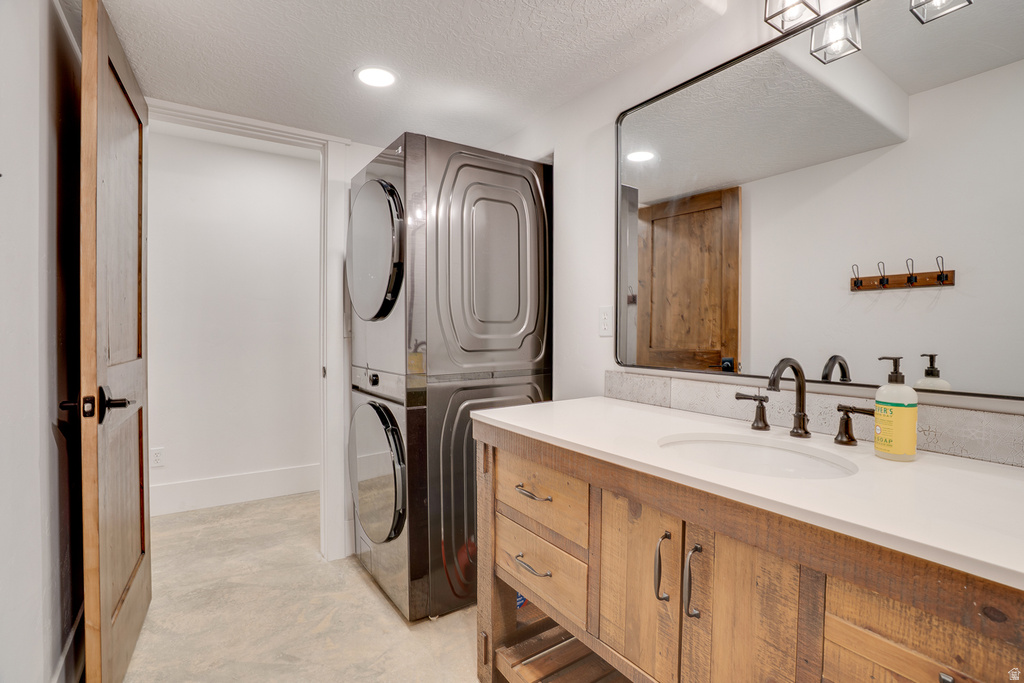 Laundry area featuring a stacked washer and dryer, wood-finish vanity with an integrated sink and white countertop, framed mirror, and dark bronze fixtures