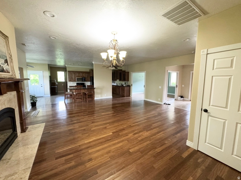 Expansive living area featuring wood-finish flooring, a decorative fireplace with a stone surround, recessed ceiling lighting, and a chandelier
