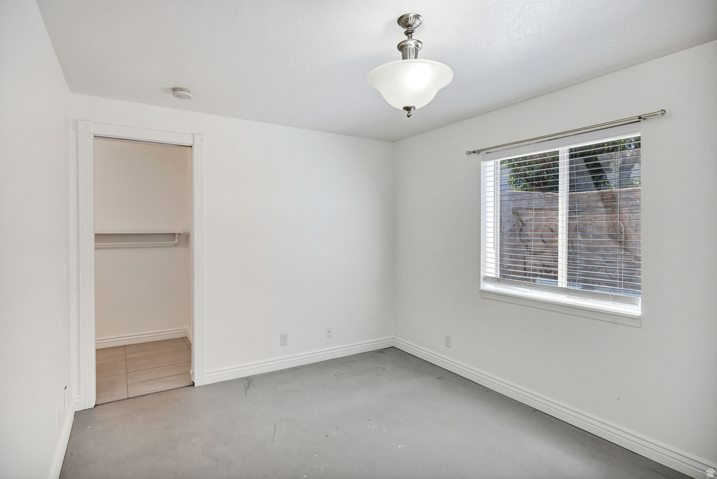Room featuring a window with blinds, a ceiling-mounted light fixture, white walls, and a closet with wood-finish flooring