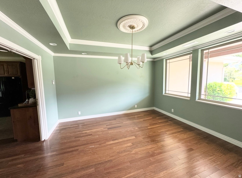 Spacious room featuring wood-finish flooring, a tray ceiling with recessed lighting, and a decorative chandelier