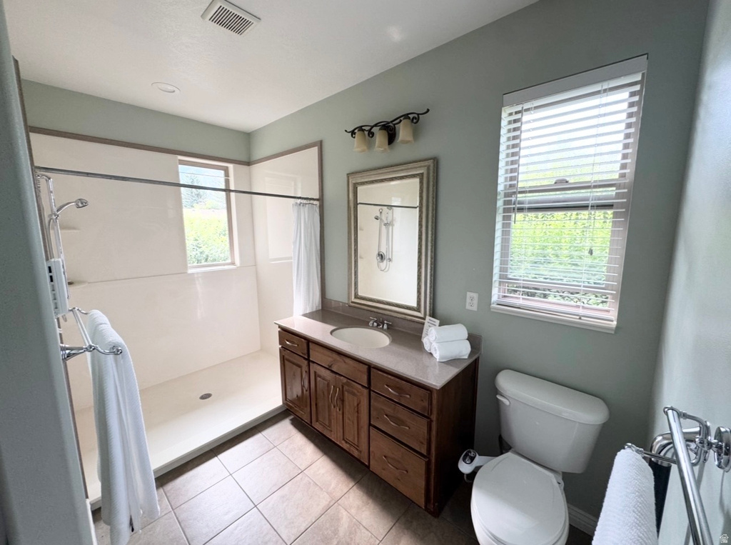 Bathroom featuring a walk-in shower with a window, a wood-finish vanity with an integrated sink, a framed mirror, and tiled flooring