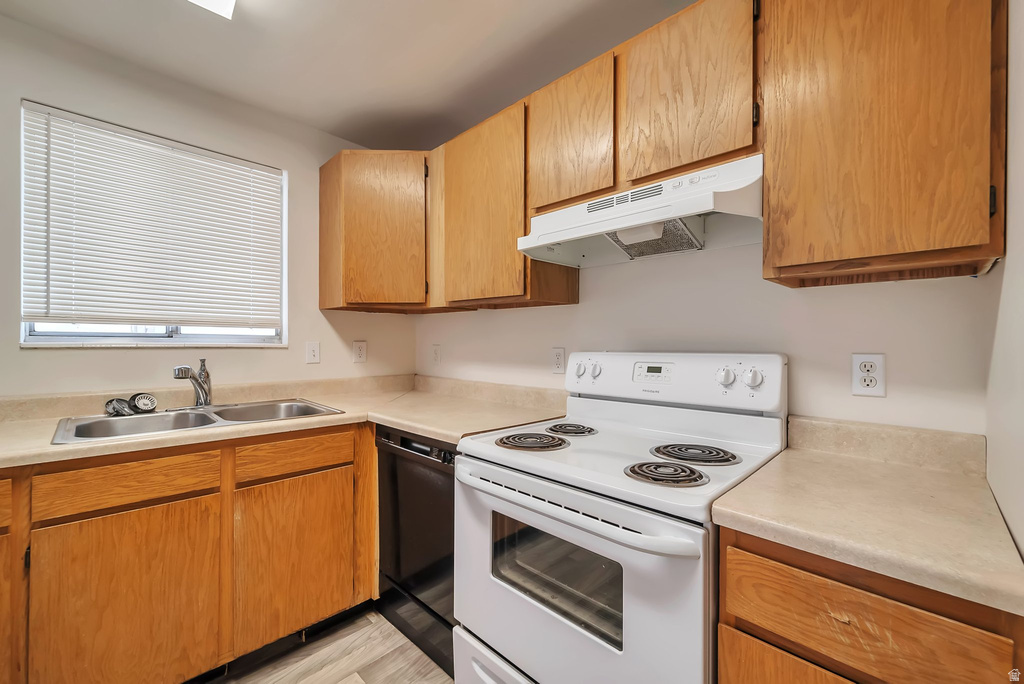 Kitchen featuring wood cabinetry, light-toned countertops, a stainless steel double sink with a chrome faucet, and a white electric range with an overhead hood