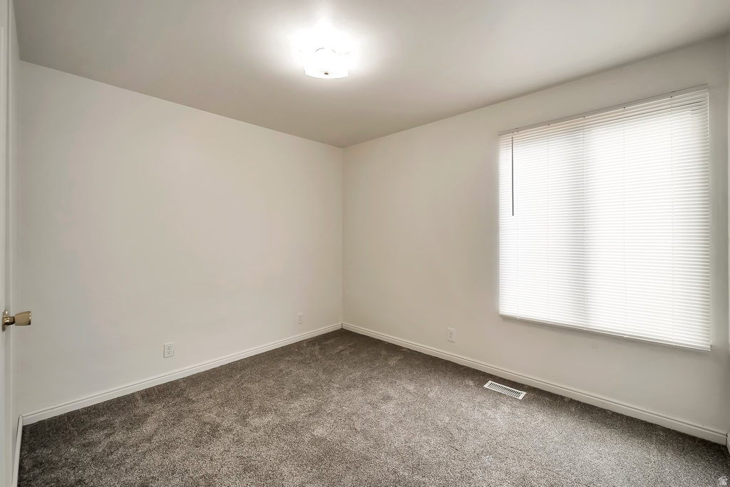 Neutral-toned room featuring a large window with horizontal blinds, gray carpet flooring, white baseboards, and a ceiling-mounted light fixture