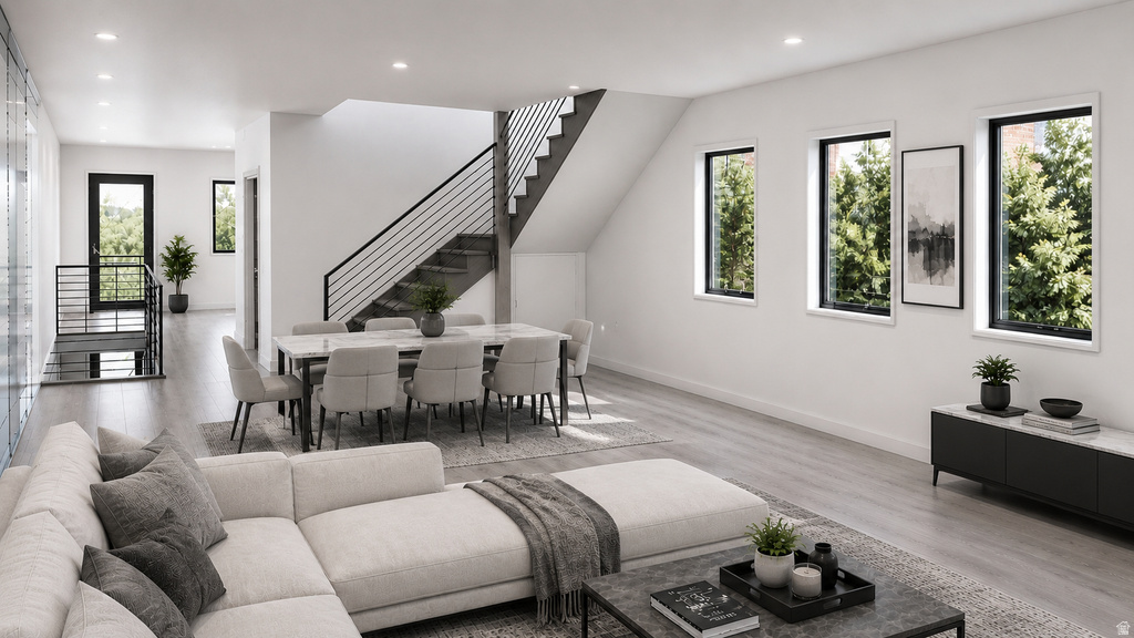 Open-concept living area featuring light wood-finish flooring, a modern black metal staircase railing, and multiple large windows with black frames