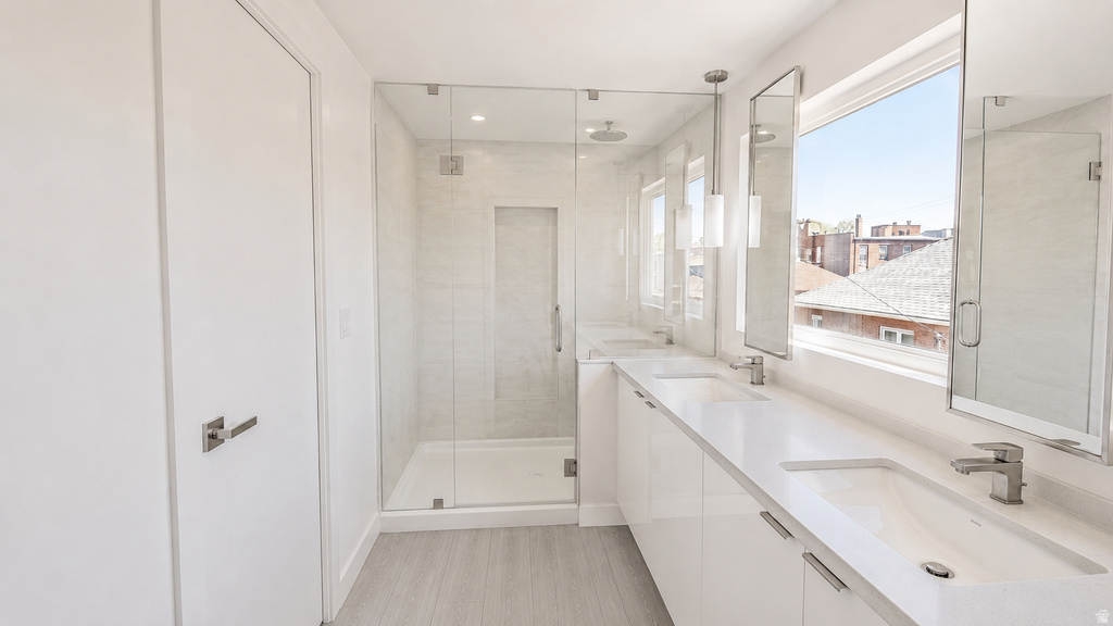 Contemporary bathroom featuring a dual vanity with undermount sinks, a spacious glass-enclosed shower, and light wood-finish flooring