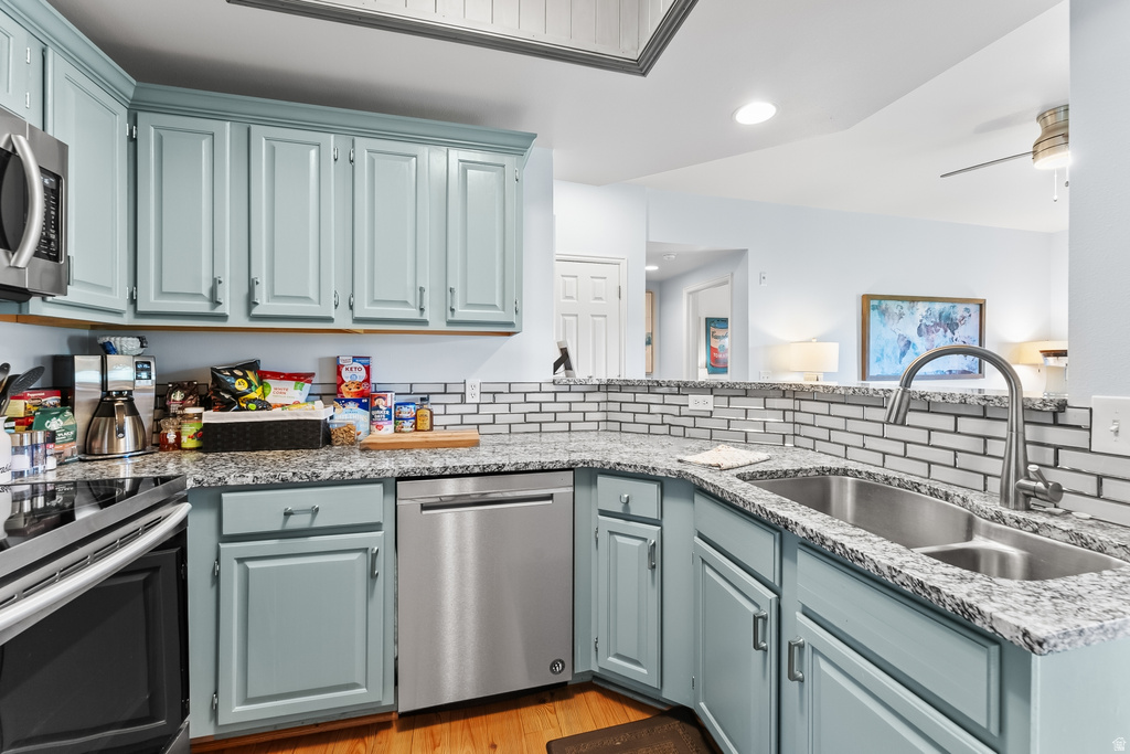 Kitchen featuring light blue cabinetry, stainless steel appliances, a double basin sink with gooseneck faucet, light-toned granite countertops, and a subway tile backsplash