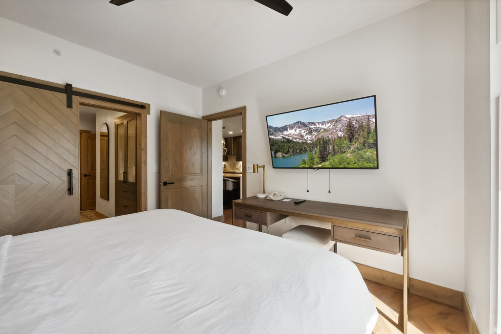 Bedroom featuring a chevron-patterned barn door, wood-finish flooring, a wall-mounted television, and a built-in desk with integrated drawers