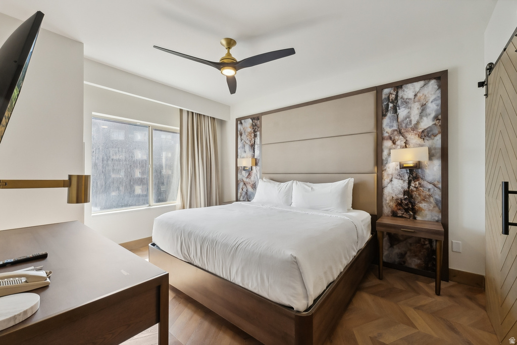 Bedroom featuring herringbone wood-finish flooring, a contemporary ceiling fan, and a paneled headboard with integrated lighting