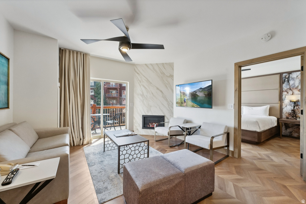 Living area featuring herringbone wood-finish flooring, a contemporary ceiling fan, and a gas fireplace with a marble-style surround