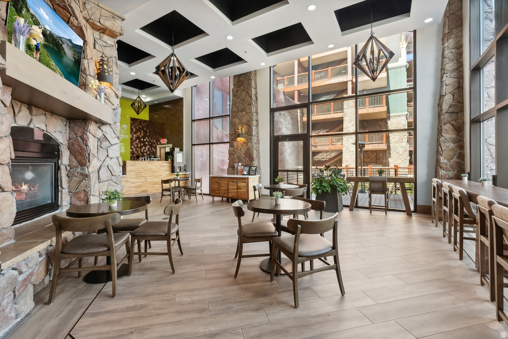 Open-concept common area featuring a stone fireplace, wood-finish flooring, full-height windows, a built-in bar, and coffered ceilings with geometric pendant lighting