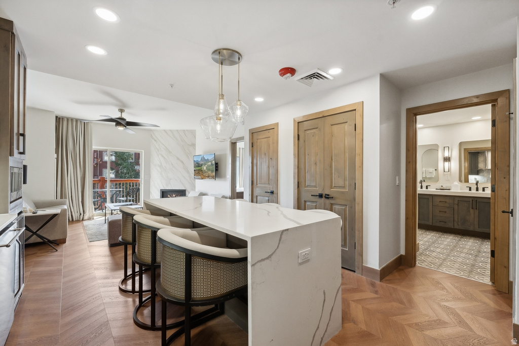 Open-concept living space with herringbone wood-finish flooring, a waterfall kitchen island with seating, pendant lighting, and a modern fireplace with a marble-look surround